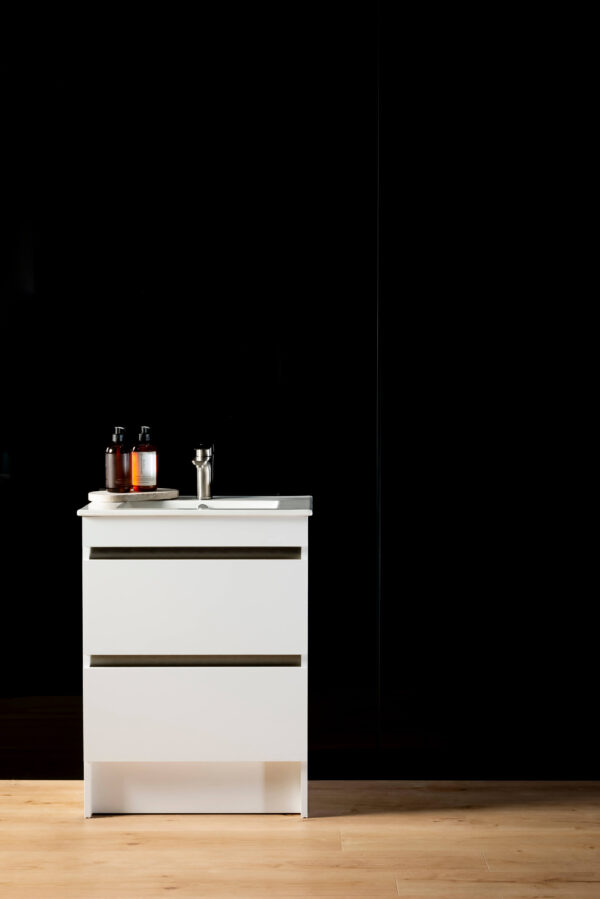 A black panel wall joined with a black joiner. A white vanity in front with soap and a wooden floor in the forefront.