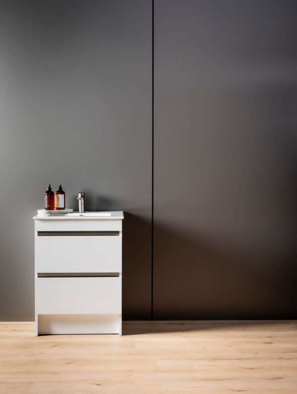 A dark grey panel wall joined with a black joiner. A white vanity in front with soap and a wooden floor in the forefront.