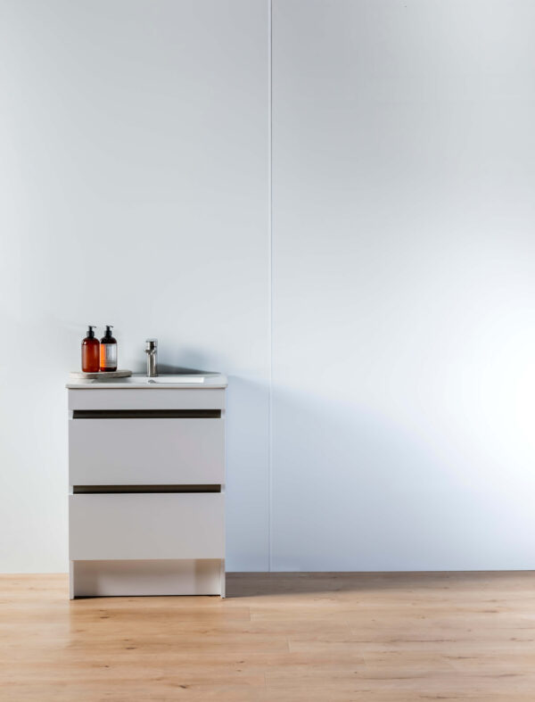 A white panel wall joined with a white joiner. A white vanity in front with soap and a wooden floor in the forefront.